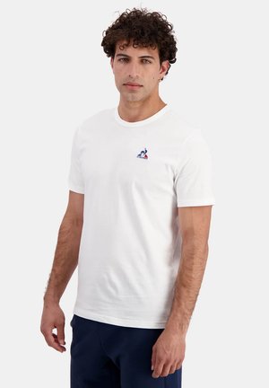 T-shirt en coton blanc avec un col rond, des manches courtes et un petit logo bleu et rouge imprimé sur la poitrine. Texture douce, coupe décontractée.