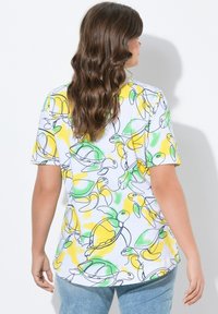T-shirt a maniche corte in bianco con una stampa colorata di una tartaruga e limoni, con accenti verdi e gialli e una vestibilità comoda.