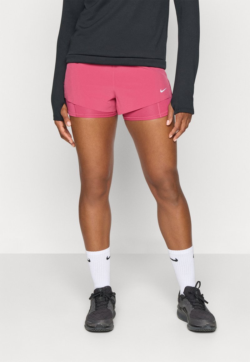 Roze sportshorts met een gebogen ontwerp en contrasterende stiksels, gecombineerd met zwarte sneakers en witte sokken met het Nike-logo.