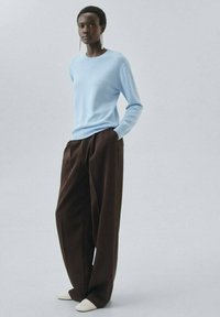 Pullover bleu clair à manches longues avec un col rond, associé à un pantalon ample marron taille haute et des chaussures blanches à bouts pointus.