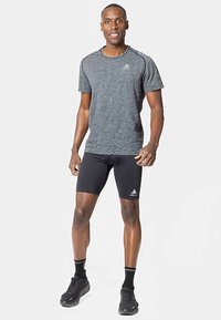 Šedé sportovní tričko s texturovanou tkaninou, v kombinaci s černými kompresními šortkami. Vzhled doplňují tenisky a sportovní ponožky.