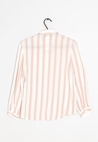 Blouse blanche transparente à rayures verticales roses, manches longues, col et poignets boutonnés. Suspendue à un cintre noir simple.