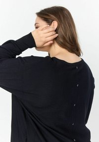Maglione nero a maglia con una vestibilità comoda, scollatura rotonda e dettagli con bottoni lungo la schiena. Tessuto morbido con maniche lunghe.