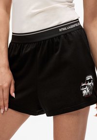 Svarta shorts med resårmidja som har en logotyp och tecknad grafik av en karaktär och en katt på vänster sida. Mjukt material.