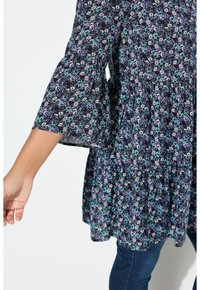 Tunic nera floreale con maniche a campana, caratterizzata da un motivo di fiori blu, bianchi e viola. Vita arricciata; tessuto leggero e testurizzato.
