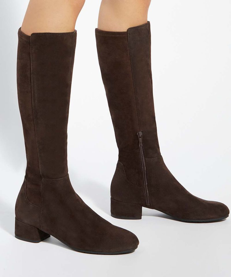 Bottes en daim marron foncé montantes jusqu'au genou avec talons blocs bas et fermetures éclair latérales, portées sur des jambes nues sur un fond uni.