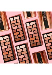 Drie rechthoekige oogschaduwpaletten, met een mix van matte en glanzende tinten in beige, roze en koper, geplaatst op een roze achtergrond.