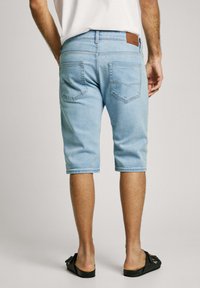 Pantalones cortos de mezclilla azul claro con un ajuste relajado, de longitud hasta la rodilla, con un acabado desgastado, que cuentan con dos bolsillos traseros y una etiqueta de cuero marrón en la cinturilla.