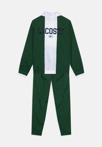 Completo sportivo verde e bianco con giacca con zip e logo "LACOSTE" e pantaloni coordinati; realizzato in tessuto leggero e liscio.