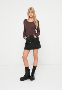 Καφέ μακρυμάνικη μπλούζα με υφή, μαύρη φούστα από ψεύτικο δέρμα με κουμπιά, μαύρα αρβυλάκια με κορδόνια και καφέ πλεκτές κάλτσες μέχρι τον αστράγαλο.