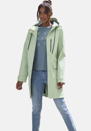 Hellgrüne, wasserdichte Jacke mit Kapuze, vorderen Druckknöpfen und verstellbaren Manschetten, getragen über einem grauen T-Shirt und kombiniert mit Jeans.