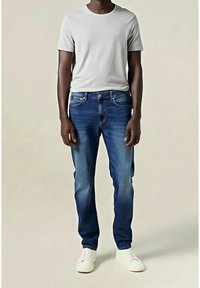 Vaaleanharmaa pyöreäkauluksinen t-paita, siniset farkut haalistuneella pesulla ja hieman kuluneisuutta, yhdistettynä valkoisiin kävelykengän.