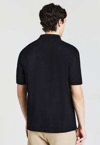 Polo nero realizzato in tessuto texturizzato, con colletto e maniche corte. Il retro presenta un design semplice senza loghi o accenti visibili.