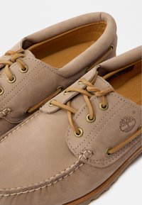 Ανοιχτό καφέ δερμάτινα παπούτσια σκάφους με καφέ κορδόνια και χρυσές βιδωτές υποδοχές. Λείος υφής, ραμμένες λεπτομέρειες και σχέδιο στρογγυλής μύτης.