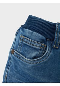 Jeans de mezclilla con una cinturilla elástica azul oscura, que presentan un bolsillo trasero con costuras naranjas y una textura desgastada.