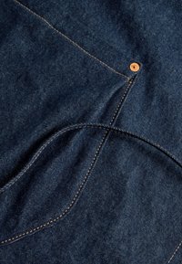 Tejido de mezclilla azul oscuro con una textura suave, costuras naranjas en contraste y un detalle de botón de cobre en el borde.