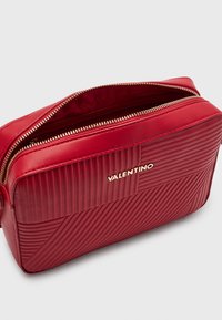 Bolso Red Valentino con líneas diagonales y verticales acolchadas, cremallera dorada parcialmente abierta y logo dorado de la marca en la parte frontal.