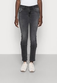 Grå tajta jeans med en slät yta, två framfickor och knäppning. Matchas med ljusa sneakers.