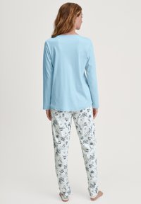 Maglietta a maniche lunghe azzurro chiaro abbinata a pantaloni da pigiama bianchi con stampa a contorno nera di vari oggetti e scene.
