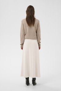 Beež kootud kampsun pika varrukaga, millele on lisatud valge, põrandapikkune, sile seelik. Komplekti täiendab mustad terava ninaga saapad.