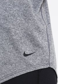 Gros plan d'un t-shirt de sport gris chiné Nike avec un logo swoosh noir près de l'ourlet, porté par-dessus un legging noir.