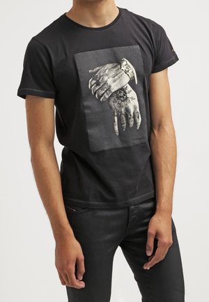 T-shirt en coton noir avec un design graphique de mains entrelacées avec des tatouages, placé dans une impression rectangulaire sur le devant.