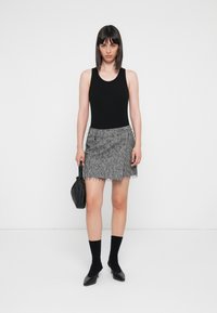 Zwarte tanktop, grijze textuur mini-jurk met franjes aan de onderkant, zwarte handtas, zwarte enkelsokken en zwart puntige hakken.