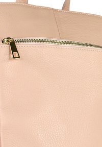 Beige leren tas met textuur, voorzien van een gouden ritsdetail en bijpassende beige handvatten.