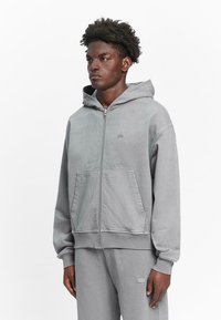Gray zip-up hoodie in soft fabric, featuring a large front pocket, ribbed cuffs, and a small logo on the chest.