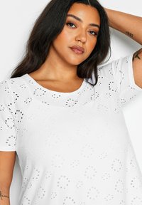 Camiseta de algodón blanca con escote redondo y mangas cortas, con un patrón texturizado de círculos perforados en toda su superficie.