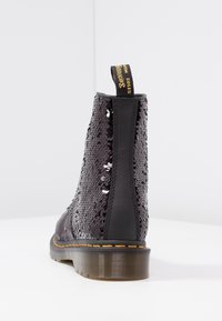 Botín de tobillo hecho de cuero negro con parte superior de lentejuelas. Presenta una suela negra gruesa y una pestaña amarilla en la parte posterior. Diseño texturizado.