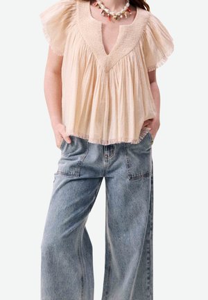 Blouse beige à manches courtes avec manches à volants, associée à un jean bleu délavé ample, taille haute, et un collier de perles imposant.