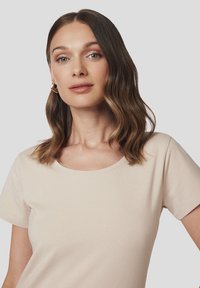 Beżowa koszulka z krótkim rękawem o okrągłym dekolcie, wykonana z miękkiego materiału, charakteryzująca się gładką fakturą i prostym wzornictwem, bez wzorów ani grafik.