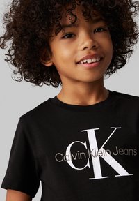 Melnas kokvilnas T-krekls ar baltu "CK Jeans" logo, īsām piedurknēm un apļa kakla dizainu. Gluda tekstūra ar minimāliem detaļām.