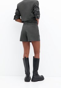 Grå shorts med en skræddersyet design, der har en baglomme. Matchet med knæ-høje sorte læderstøvler med en kraftig sål.