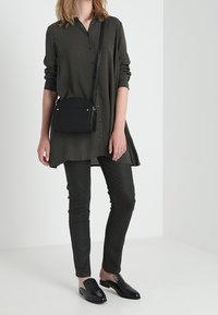 Tunica lunga a pois bianchi e neri con colletto, abbinata a pantaloni neri slim e scarpe nere stringate. Semplice borsa a tracolla nera.