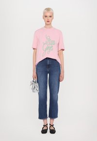 T-shirt de algodão rosa com gráfico em verde, jeans azul, sapatilhas pretas com bolinhas e uma mini bolsa transparente. Vista frontal, fundo neutro.