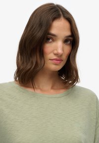 Lys grøn t-shirt med afslappet pasform, rund halsudskæring og subtil struktur; har et lille broderet logo på brystet.