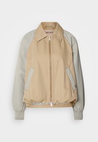 Veste beige à fermeture éclair sur le devant, manches raglan gris clair et bordures de poches assorties, poignets élastiques et col plat.