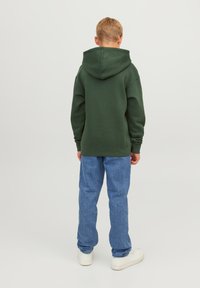 Sudadera con capucha de color verde oscuro con un bolsillo tipo canguro, combinada con jeans de mezclilla azul claro y zapatillas blancas. Diseño casual y de corte relajado.