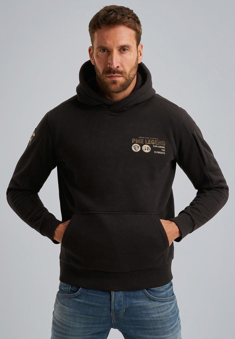 Sweatshirt à capuche noire en mélange de coton avec une poche kangourou sur le devant. Présente un texte doré et des logos sur la poitrine et la manche gauche.