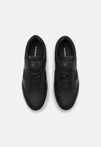 Svarta sneakers med ett strukturerat läderöverdrag, runda snören, ett vadderat inre och en vit gummisula. G-Star Raw-logotyp synlig.