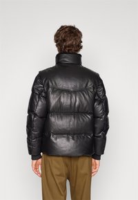 Svart läderpuffjacka med hög krage, kviltad design, ribbad mudd och strukturerad siluett, kombinerad med khakifärgade byxor.