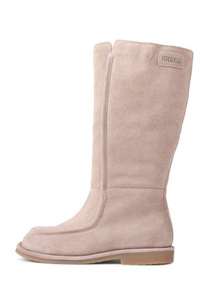 Beige mokkaseni joka yltää polveen, jossa on sileä pinta, pyöristetty kärki ja minimaalinen ommel. Varustettu litteällä kumipohjalla ja brändätyllä tarralla.