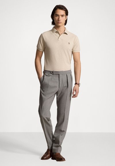 Beige polo skjorte med et lite emblem, kombinert med skreddersydde grå bukser med frontfalter og dobbelte knapper. Brune dressko.