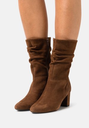 Bottines en daim marron avec un design décontracté, bout pointu et talon épais. Équipées d'une fermeture à glissière sur le côté pour un enfilage facile. Texture lisse.