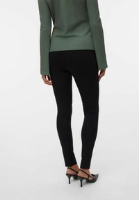 Svarta leggings med en åtsittande design och en slät textur. Kombineras med en grönt topp med textur och svarta klackar med en smal rem.