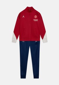 Sarkana sporta jaka ar baltām piedurknēm un logo, savienota ar tumši ziliem biksiem ar logo detalēm. Izgatavota no gludas, sportiskas auduma.