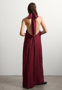 Burgunderfarbene Halter-Rücken-Kleid mit einer gebundenen Schleifendetail, aus strukturiertem Stoff gefertigt, mit offenem Rücken und bodenlanger Gestaltung.