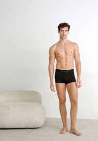 Caleçons boxers noirs avec le logo Calvin Klein, fabriqués à partir d'un tissu lisse, présentés sur un mannequin masculin devant un fond uni.